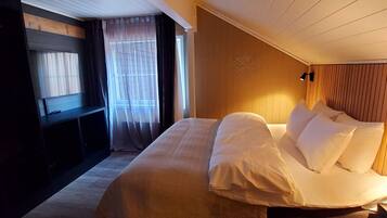 A bedroom with a large bed, a wooden headboard, a bedside table, and a window with curtains.