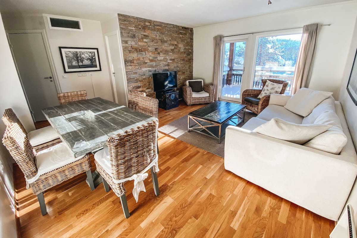A living room with a stone wall, a dining table with chairs, a sofa, and a TV.