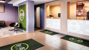 A hotel reception area with a modern design, featuring a reception desk, seating area, and a green wall with a logo. - B&B Hotel Kaiserslautern (Kaiserslautern)