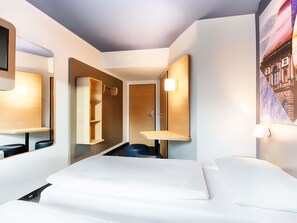 Una habitación de hotel moderna con cama, espejo, estante de madera y luz empotrada en la pared.
