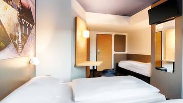 Ein Hotelzimmer mit zwei Betten, einem kleinen Tisch, einem Spiegel und einem am Wand montierten Fernseher.