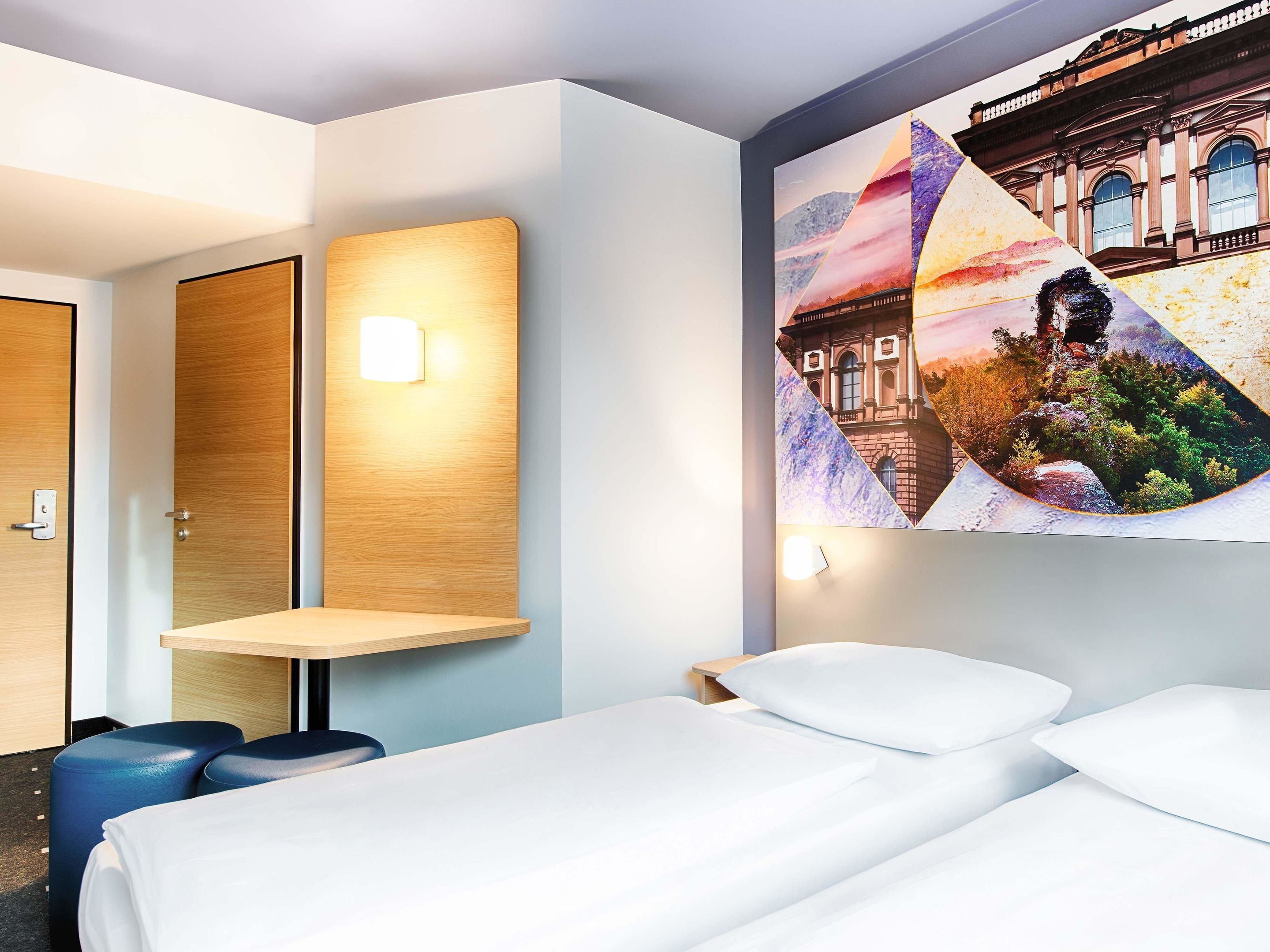 A hotel room with a bed, a desk, and a wall-mounted artwork.