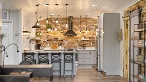 Une cuisine moderne avec un mur de fond en briques, des luminaires suspendus et un îlot central doté de tabourets de bar.
