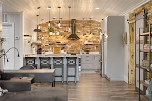 Una cucina moderna con rivestimento in mattoni, luci a sospensione e un'isola centrale con sgabelli da bar.