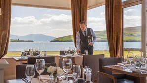 A restaurant with tables set for dining, a waiter attending to guests, and a scenic view of a lake and hills. - Dingle Skellig (Dingle)