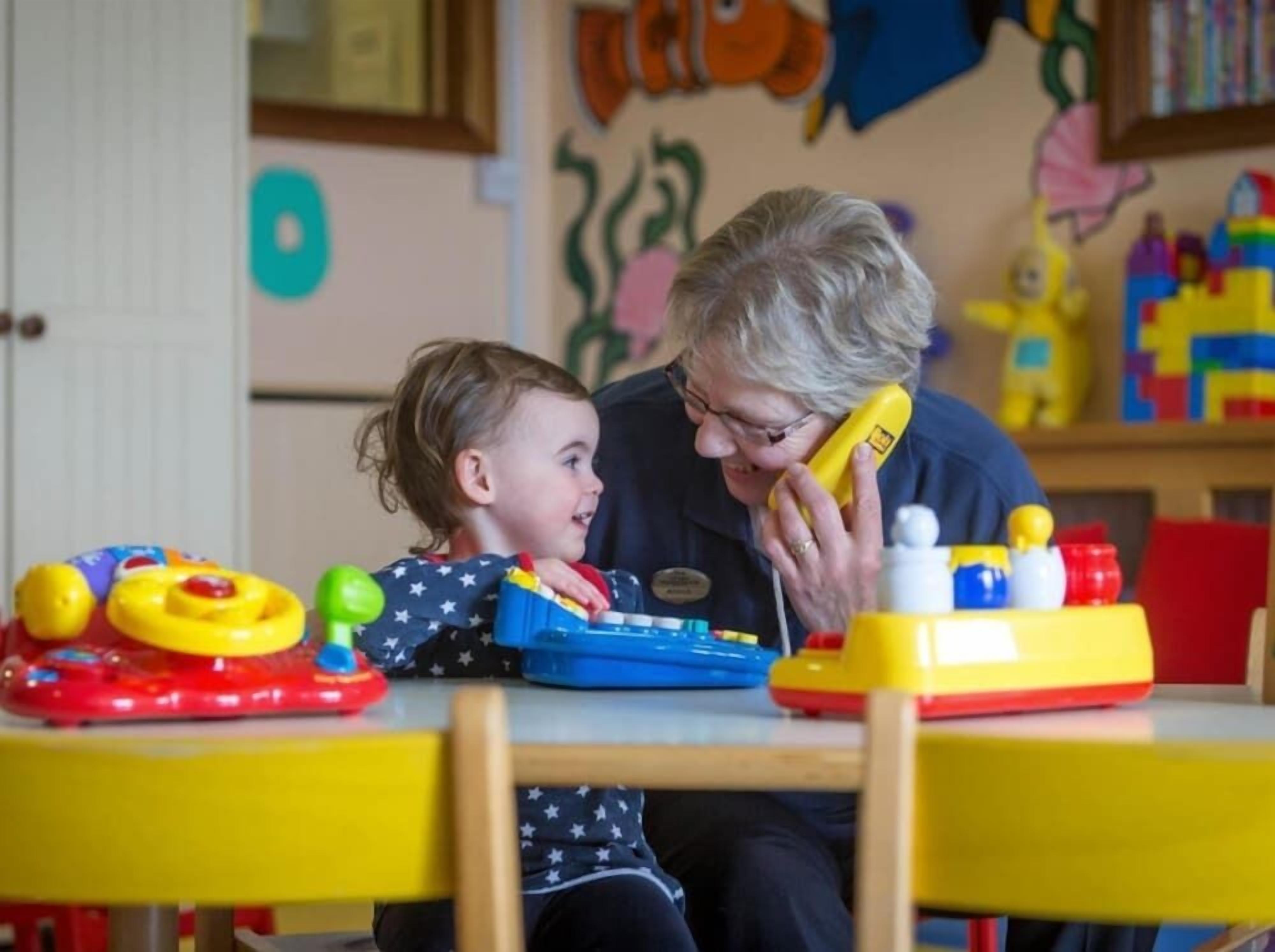 A child and an adult at a table with toys and a telephone.