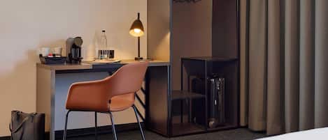 Habitación de hotel con escritorio, silla, cama y vestidor con ropa colgada.