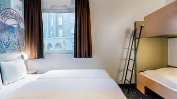 Una habitación de hotel con una cama grande, una cama más pequeña, una ventana con cortinas, una escalera y un cuadro de un paisaje urbano en la pared.