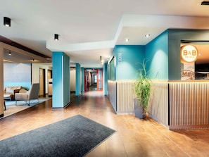 Un espace d’accueil moderne, comprenant un comptoir de réception, un coin salon avec un canapé et une plante en pot.