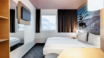 Ein Hotelzimmer mit Bett, Fernseher, Fenster mit Vorhängen, einem Gemälde und einer Lampe.