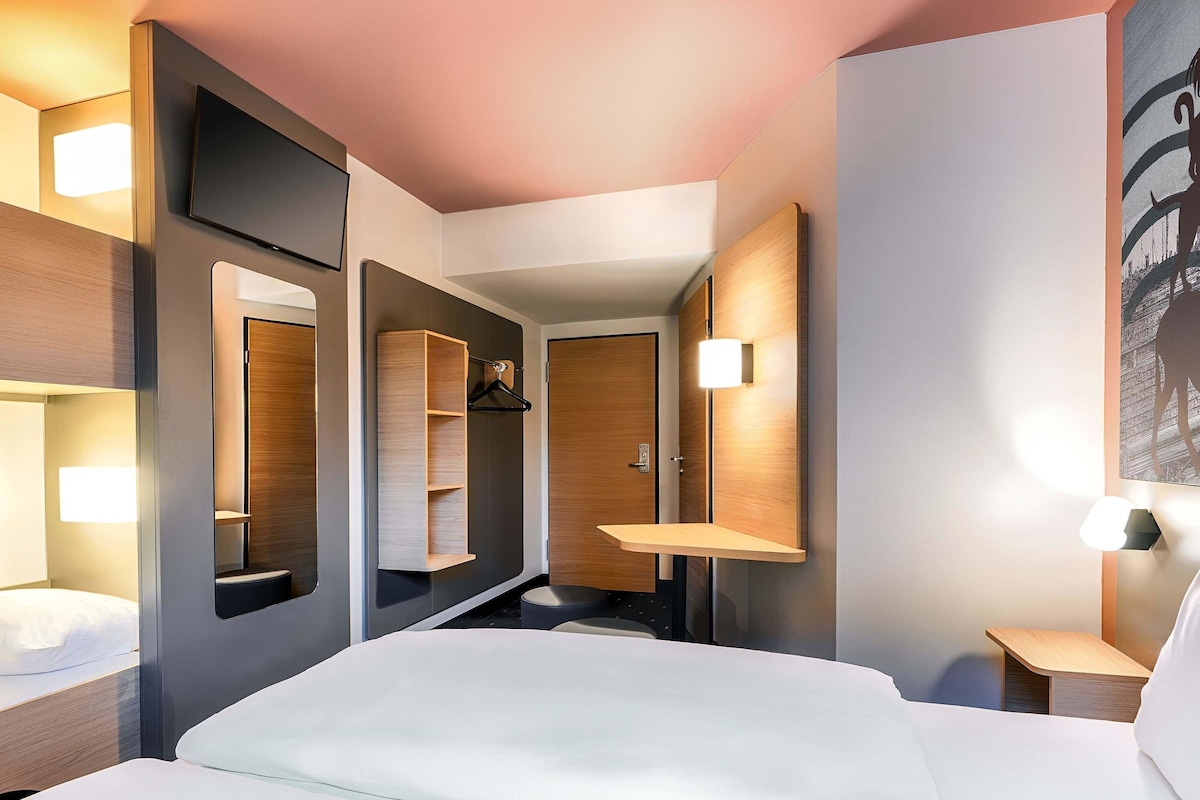 Une chambre d’hôtel moderne avec un grand lit, une armoire, un miroir et une petite table de chevet.