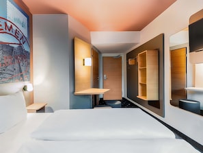 Une chambre d’hôtel moderne dotée d’un grand lit, d’étagères intégrées, d’une porte avec une poignée et d’un luminaire fixé au mur.