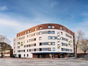 Un hôtel moderne à la façade incurvée, doté de nombreuses fenêtres et d’une enseigne bien visible.