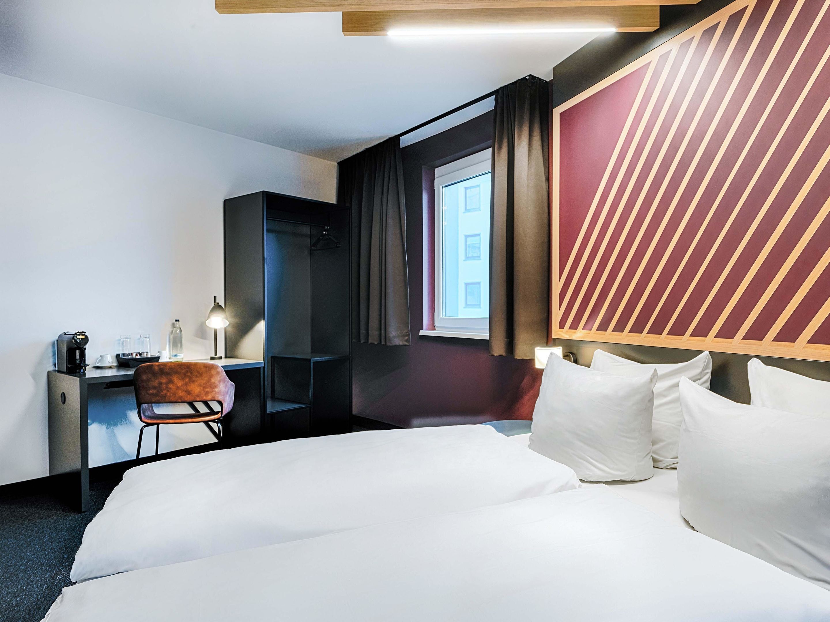 Une chambre d’hôtel avec un grand lit, un bureau avec une chaise, une armoire et une fenêtre avec des rideaux.
