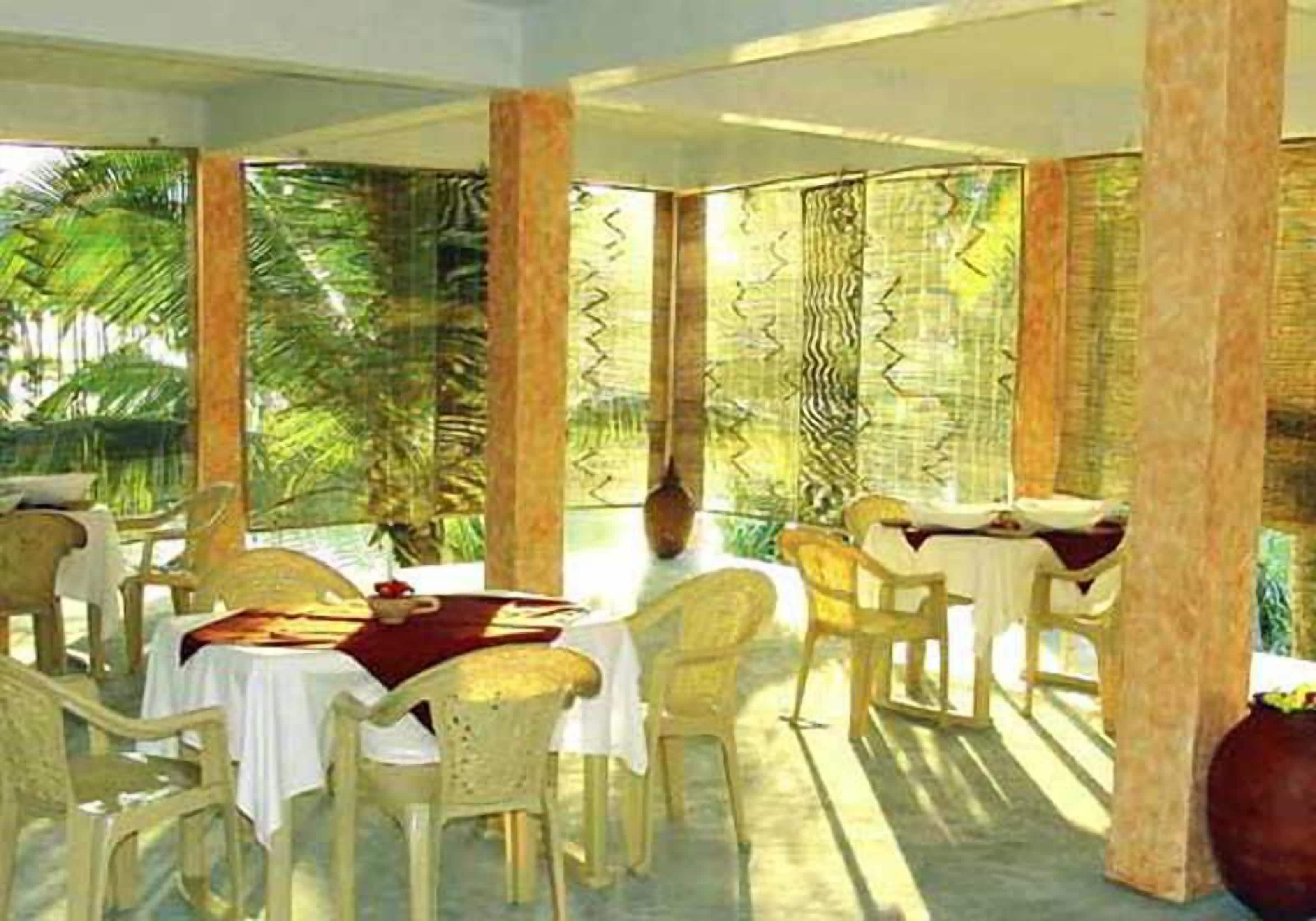 A dining area with tables and chairs, large windows, and a view of palm trees.