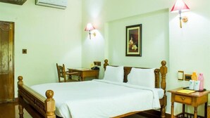 Une chambre d’hôtel avec un lit en bois, un bureau, une chaise, une table de chevet et une lampe fixée au mur.