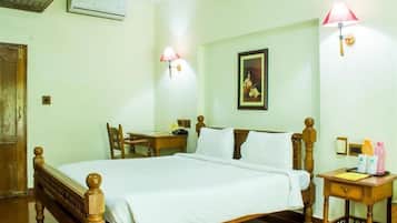 A hotel room with a wooden bed, a desk, a chair, a nightstand, and a wall-mounted lamp.