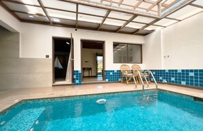 An indoor swimming pool with clear blue water, a sunroof, and a seating area with two chairs. - Isola di Cocco Ayurvedic Beach Resort (Neyyattinkara)