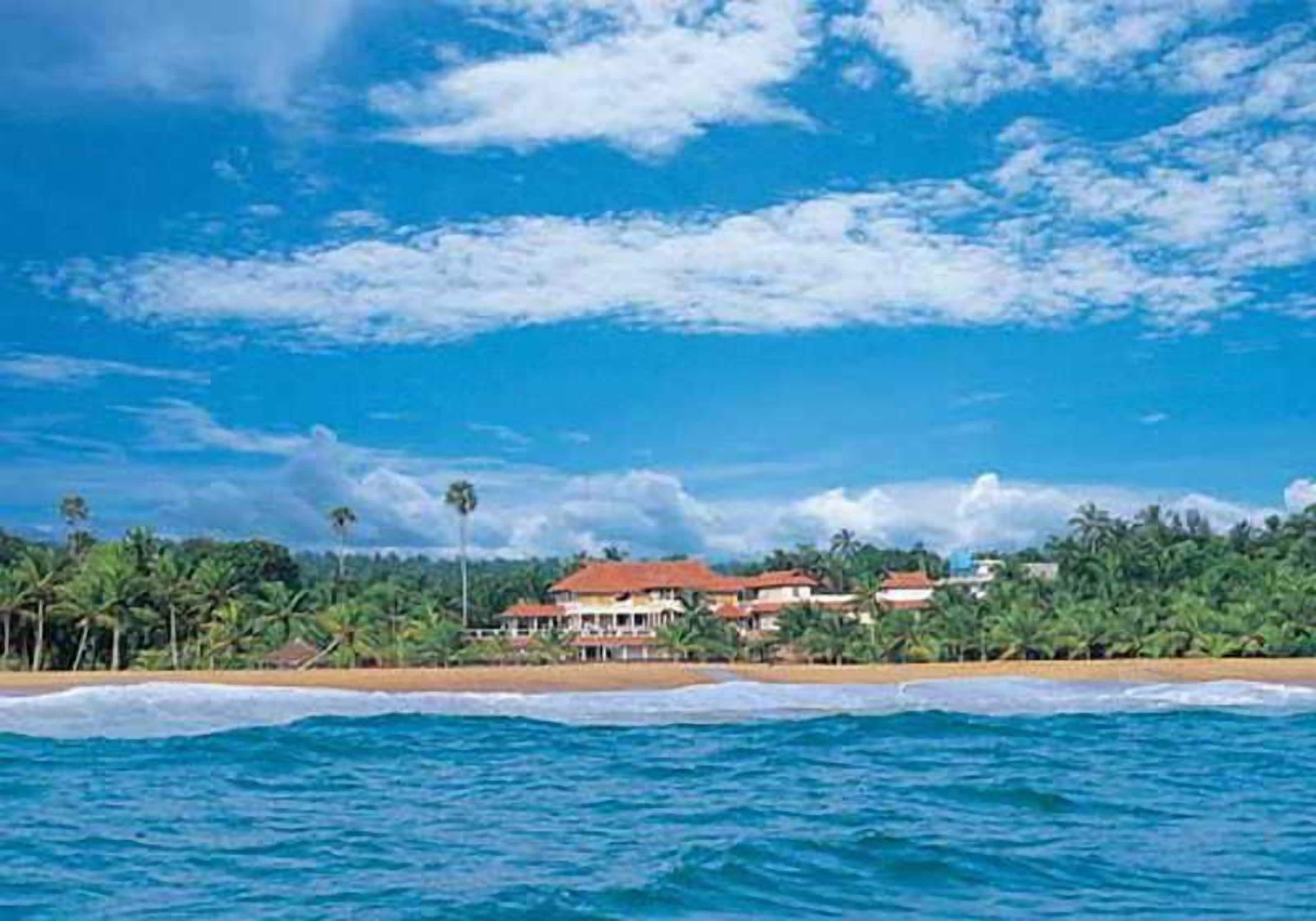A beachfront property with a large building, palm trees, and ocean waves.