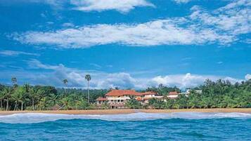 A beachfront property with a large building, palm trees, and ocean waves.