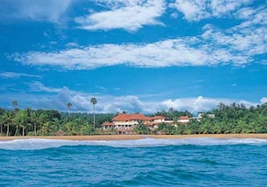 A beachfront property with a large building, palm trees, and ocean waves.