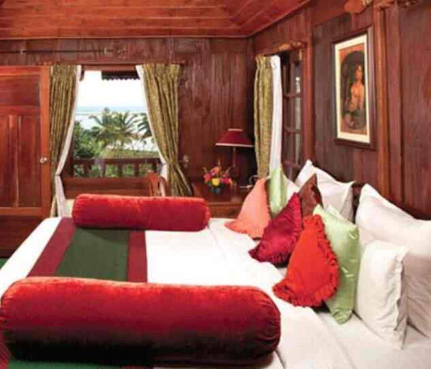 A wooden room with a bed, pillows, a window with curtains, and a painting on the wall.