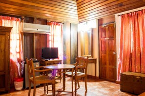 A room with wooden panel walls, a television, a round wooden table with chairs, and a wooden cabinet. - Isola di Cocco Ayurvedic Beach Resort (Neyyattinkara)