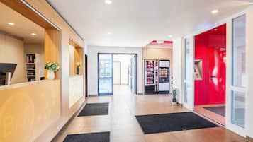 A modern hotel lobby with a reception desk, a vending machine, and a red accent wall.
