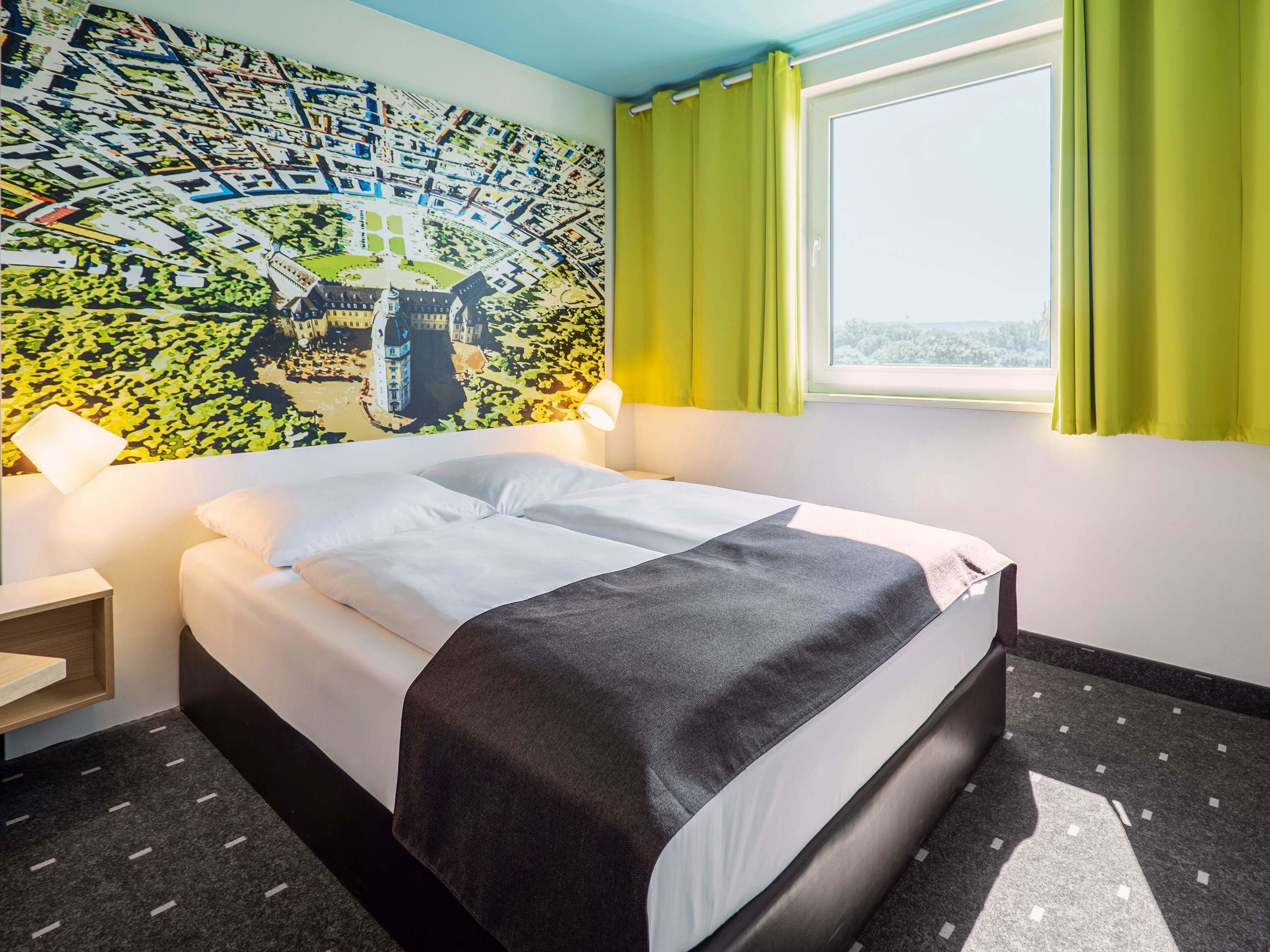 A hotel room with a bed, a map mural, a window with curtains, and a nightstand.