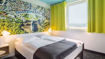 A hotel room with a bed, a map mural, a window with curtains, and a nightstand.