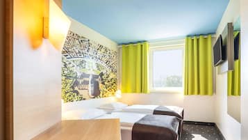 Ein Hotelzimmer mit Bett, Schreibtisch, Stuhl, einem Fenster mit Vorhängen und einem am Wand befestigten Fernseher.