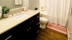 Un baño con lavamanos doble, inodoro, cortina de ducha y una pequeña planta en maceta.