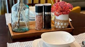 Una mesa de comedor con un florero de flores blancas, saleros y una botella de vidrio.