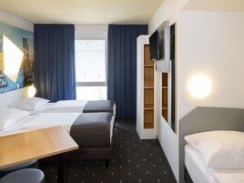 Una habitación de hotel con dos camas, un escritorio, una silla, un televisor y una ventana con cortinas.