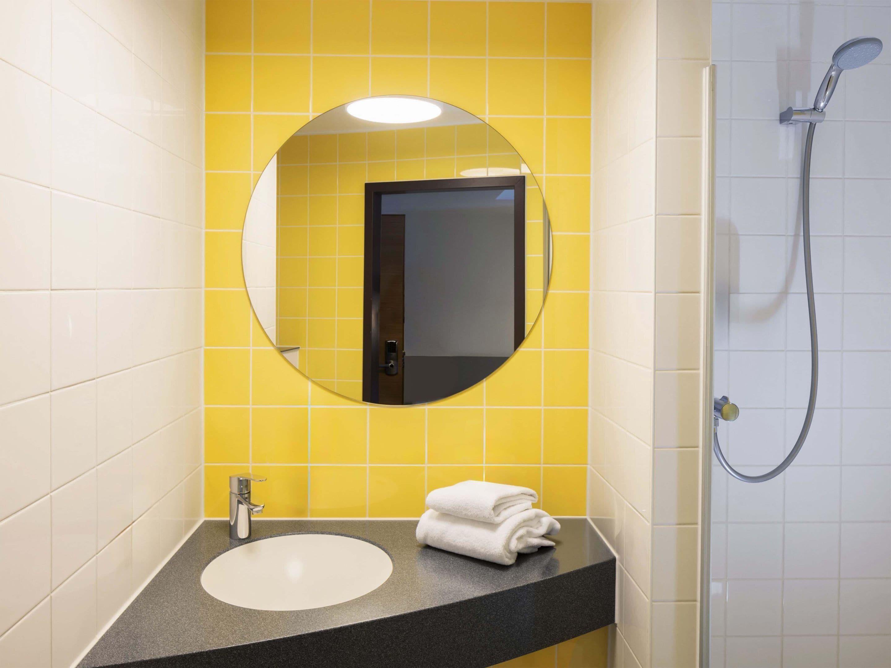 Un baño con espejo redondo, lavamanos y ducha.