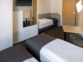Habitación de hotel con dos camas, un escritorio, una silla y un televisor instalado en la pared.