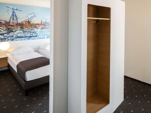 Habitación de hotel con cama, armario de madera y un mural de paisaje urbano en la pared.