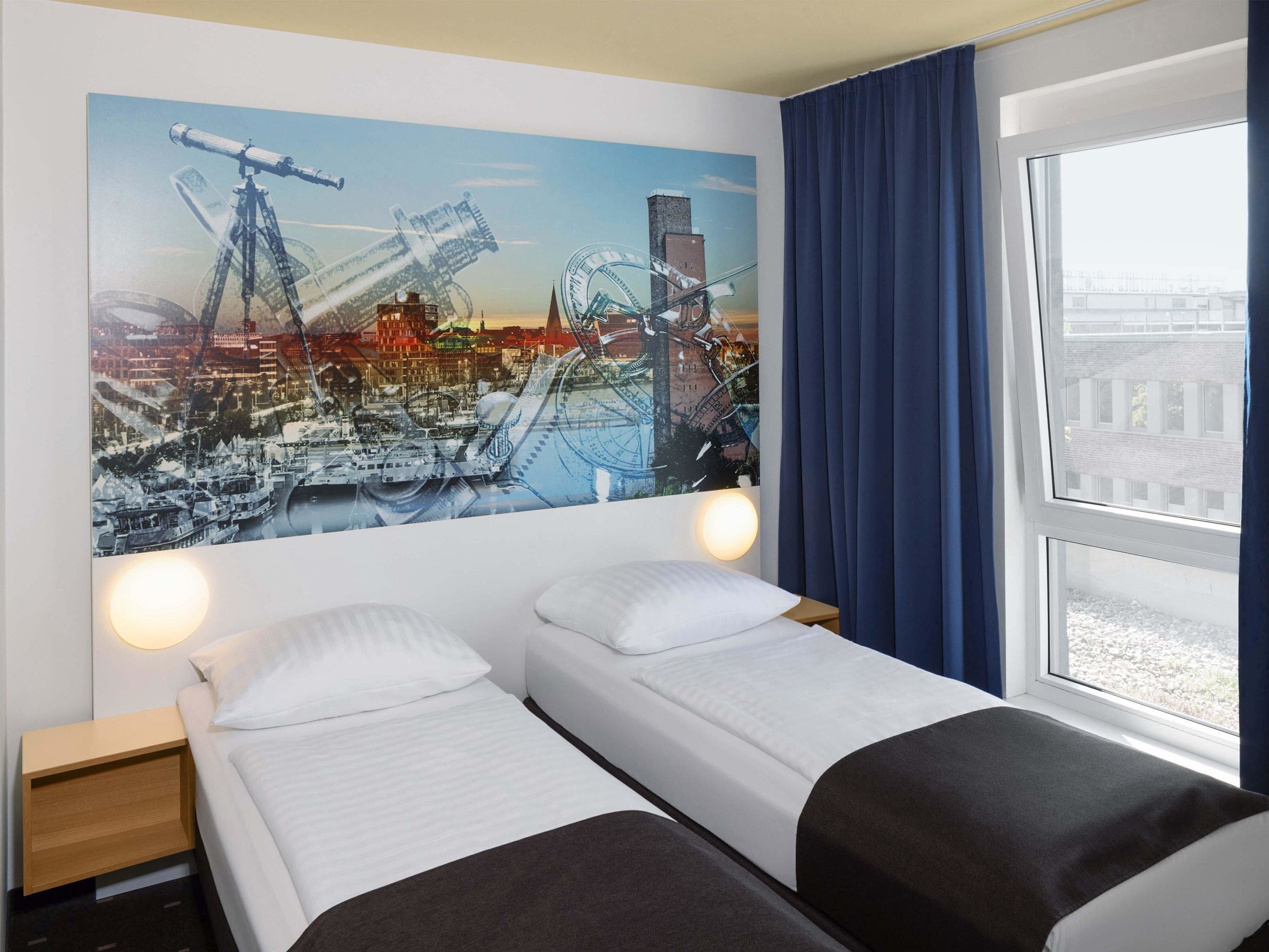 Ein Hotelzimmer mit zwei Betten, einem Stadtbild-Wandgemälde, einem Fenster mit Vorhängen und einem Nachttisch.