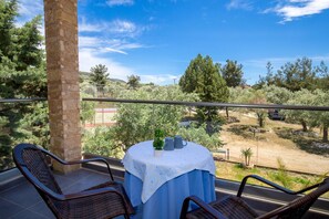 A balcony with wicker chairs, a table with a blue tablecloth, and a view of trees and a road. - Astris Sun (Thasos)