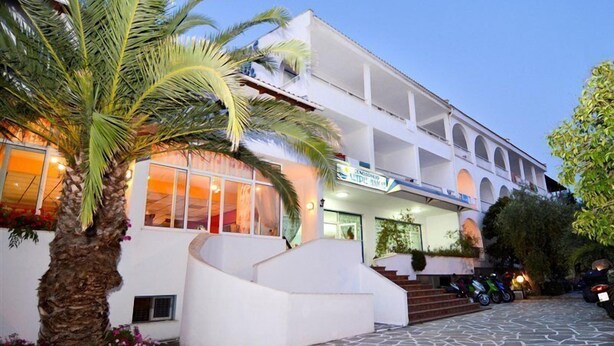 A hotel with a white facade, a palm tree, and a stone-paved courtyard. - Astris Sun (Thasos)