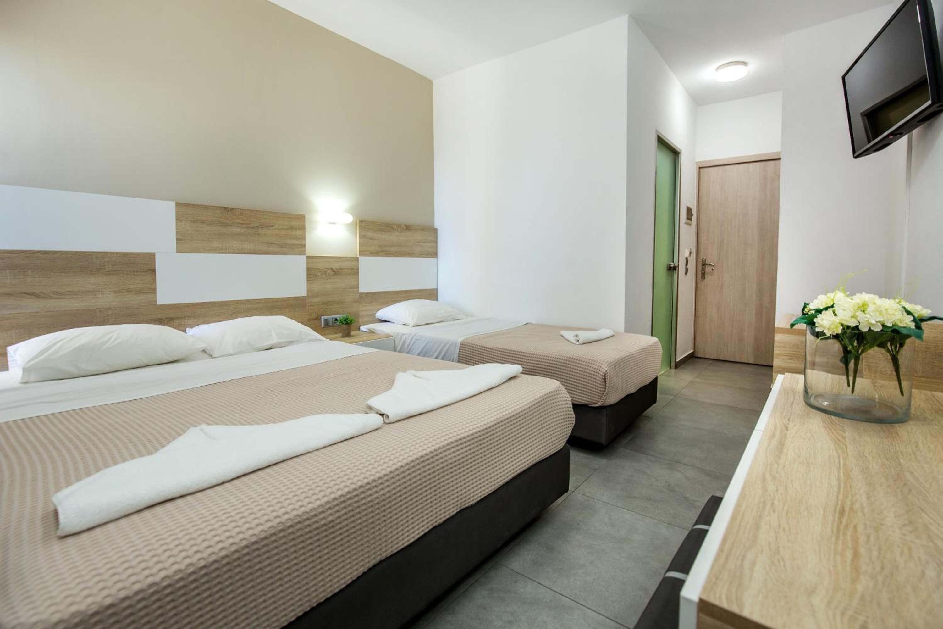 Ein Hotelzimmer mit zwei Betten, einem an der Wand montierten Fernseher und einer grünen Tür.