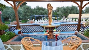 An outdoor pool area with lounge chairs, a table with chairs, and a decorative fountain. - Astris Sun (Thasos)