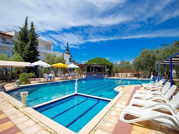 A swimming pool with lounge chairs and umbrellas, surrounded by buildings and trees.
