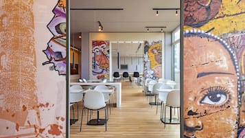 A modern dining area with white tables and chairs, a wooden floor, and colorful murals on the walls.