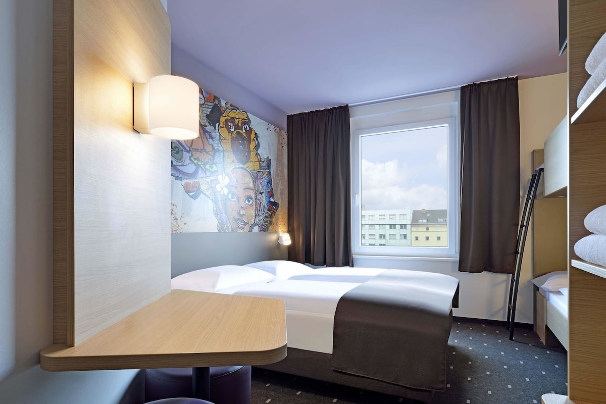 Hotellihuone, jossa on sänky, työpöytä, tuoli, ikkuna verhoilla ja taulu seinällä.