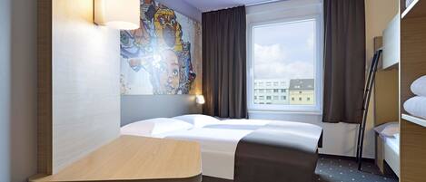 Une chambre d’hôtel avec un lit, un bureau, une chaise, une fenêtre avec des rideaux et un tableau au mur.