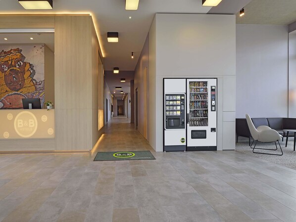 Uma área de recepção de hotel com uma máquina de vendas automática, um balcão de atendimento e uma área de estar.