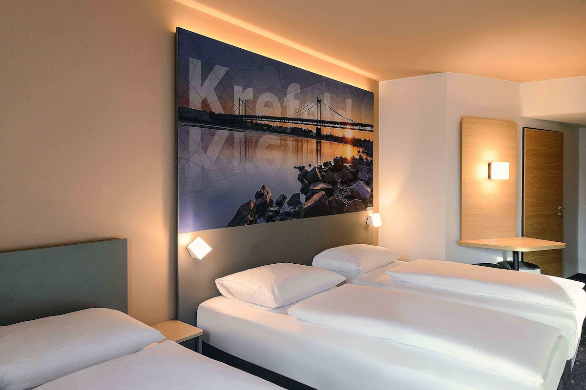 Une chambre d’hôtel avec deux lits, une grande œuvre d’art représentant un pont, accrochée au mur, et une table de chevet avec une lampe.