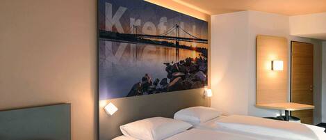 Ein Hotelzimmer mit zwei Betten, einem großen Wandbild einer Brücke und einem Nachttisch mit einer Lampe.