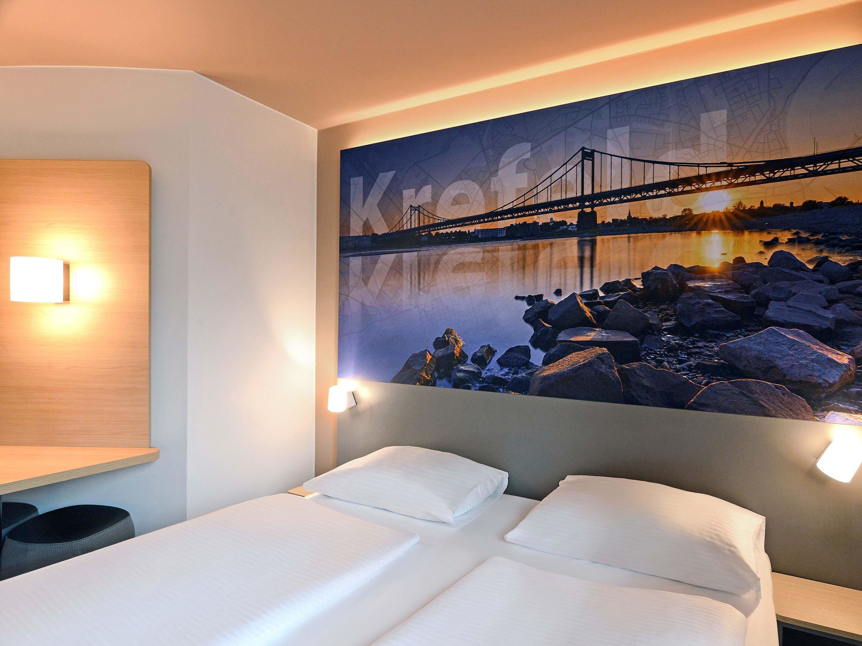 A hotel room with a bed, a wall-mounted light, and a large cityscape mural.